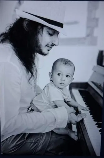 Maxma at the piano with a baby on his lap